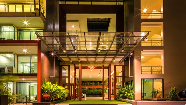 A modern hotel entrance with a glass canopy, multiple floors, and indoor plants. - At The Tree Phuket (Rawai)