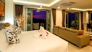 A modern hotel room with a large bed, a sofa, a balcony with a city view, and a dining area. - At The Tree Phuket (Rawai)