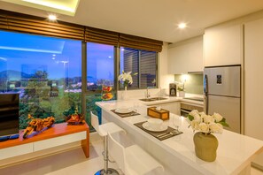 A modern kitchen with a large island, stainless steel appliances, and a view of the cityscape. - At The Tree Phuket (Rawai)