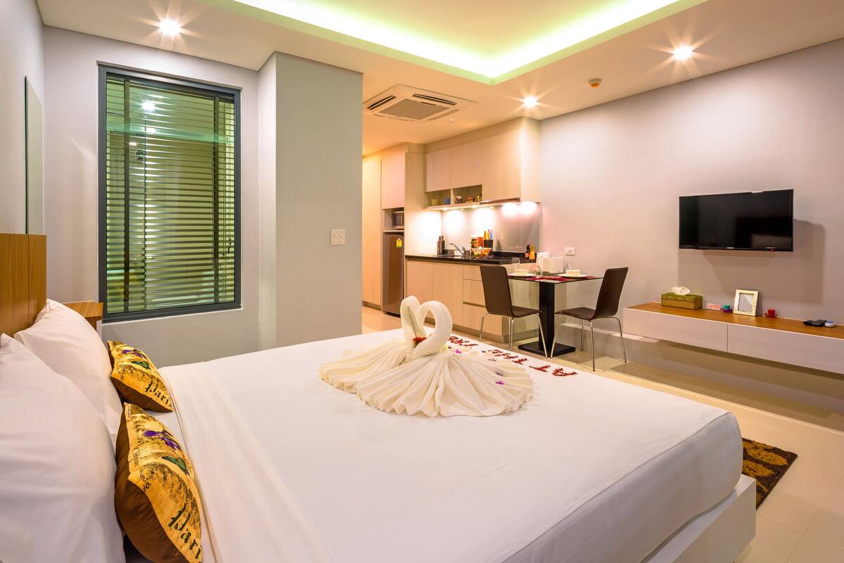 A hotel room with a bed, a TV, a desk, and a kitchenette.