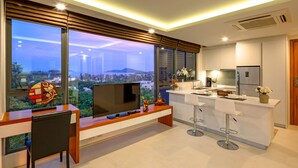A modern kitchen with a large island, bar stools, and a TV on a wooden console. - At The Tree Phuket (Rawai)