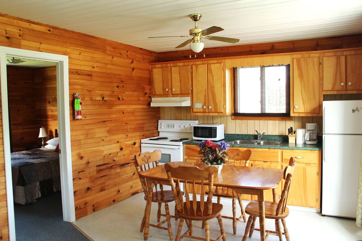 Eine Holzhütte mit einer Küche, ausgestattet mit Holzausbau, einem Herd, einer Mikrowelle, einem Kühlschrank und einem Esstisch mit Stühlen.