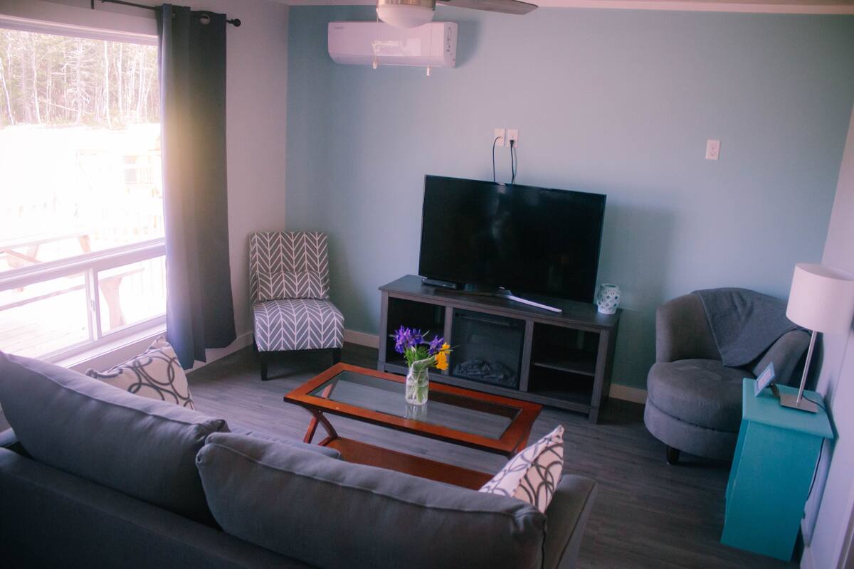 Ein Wohnzimmer mit einer Couch, einem Couchtisch, einem Fernseher, einem gemusterten Sessel und einem Türkistabl.