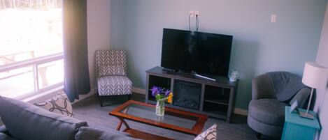 A living room with a sofa, a coffee table, a TV, a patterned chair, and a teal side table.