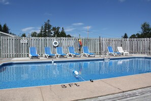 A swimming pool with 8 blue and white lounge chairs, a shallow area sign, and a 3 ft depth marking.