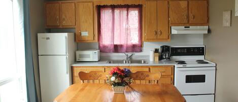 A kitchen with wooden cabinets, a white refrigerator, a microwave, a stove, and a dining table with chairs.