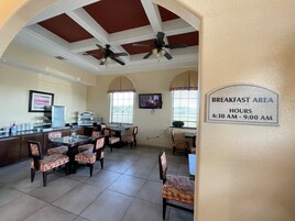 A breakfast area with ceiling fans, a coffee station, and a sign indicating breakfast hours from 6:30 AM to 9:00 AM.