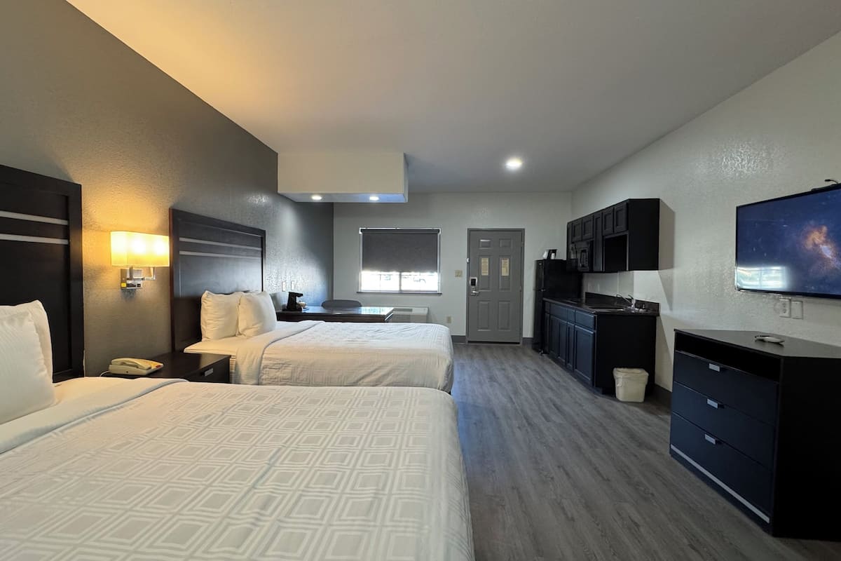 A hotel room with two beds, a desk, a TV, and a kitchenette.