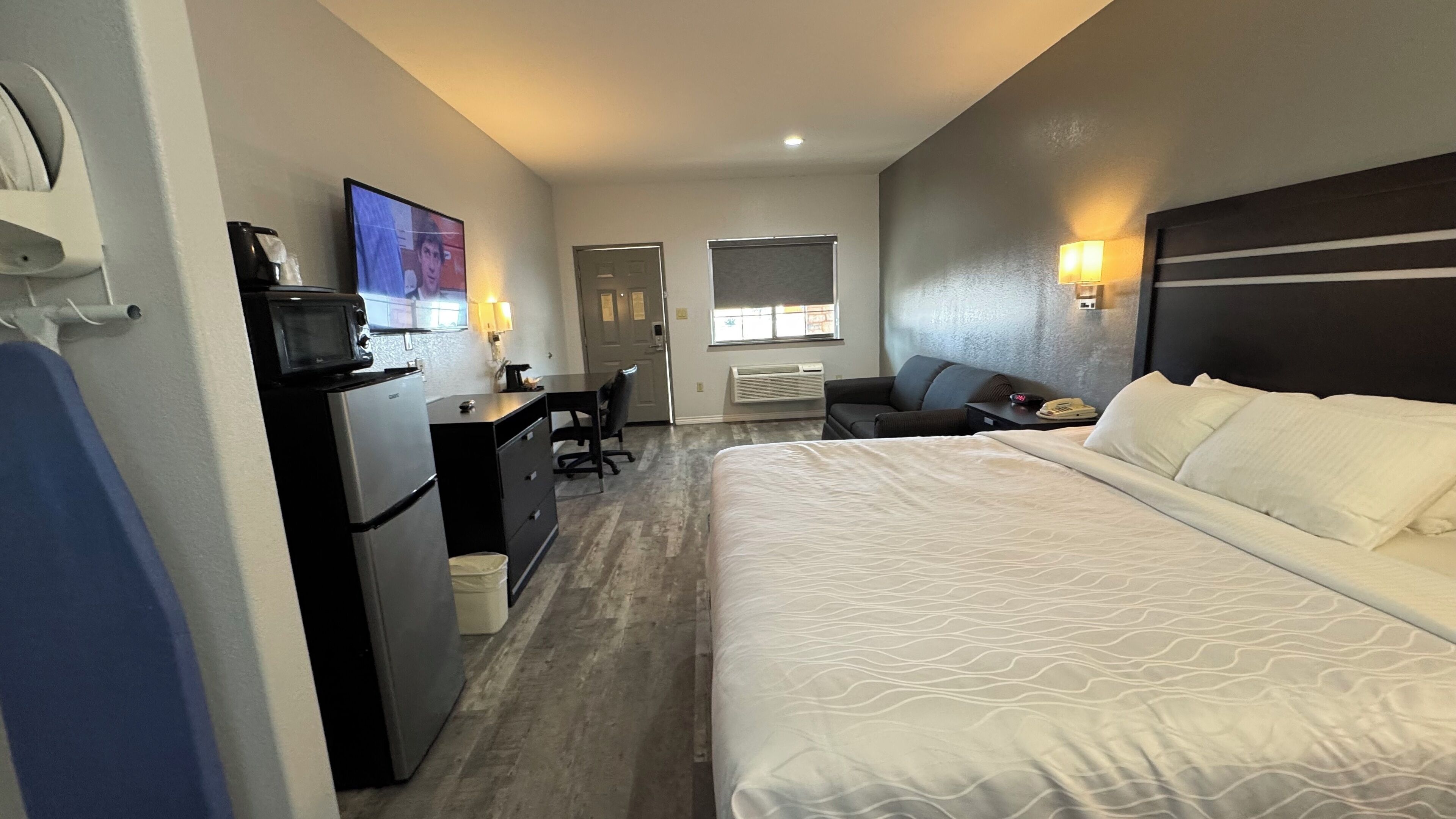 A hotel room with a bed, desk, chair, microwave, and a television.