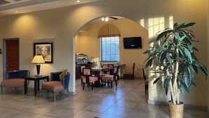 A spacious living area with a dining set, a large potted plant, and a TV mounted on the wall. - Sunbridge Inn and Suites (Jourdanton)