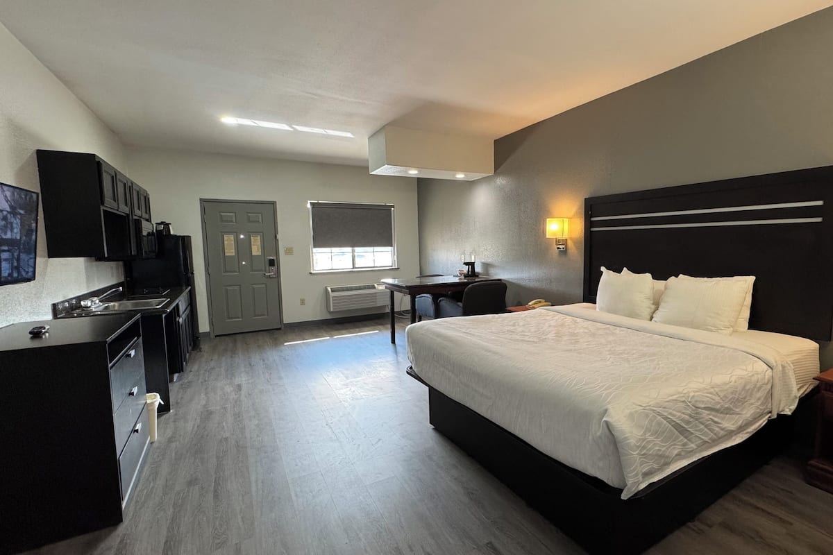 A hotel room with a bed, bedside table, desk, and kitchenette.