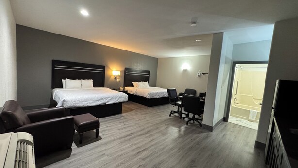 A hotel room with two beds, a desk, a chair, and a small table. - Sunbridge Inn and Suites (Jourdanton)