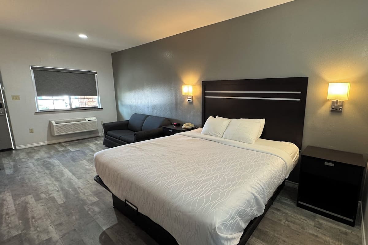 A modern hotel room with a large bed, a sofa, a bedside table, and a nightstand.