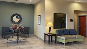 A lobby with a reception desk, two sofas, a coffee table, a lamp, a mirror, and a door labeled "Business Center". - Sunbridge Inn and Suites (Jourdanton)