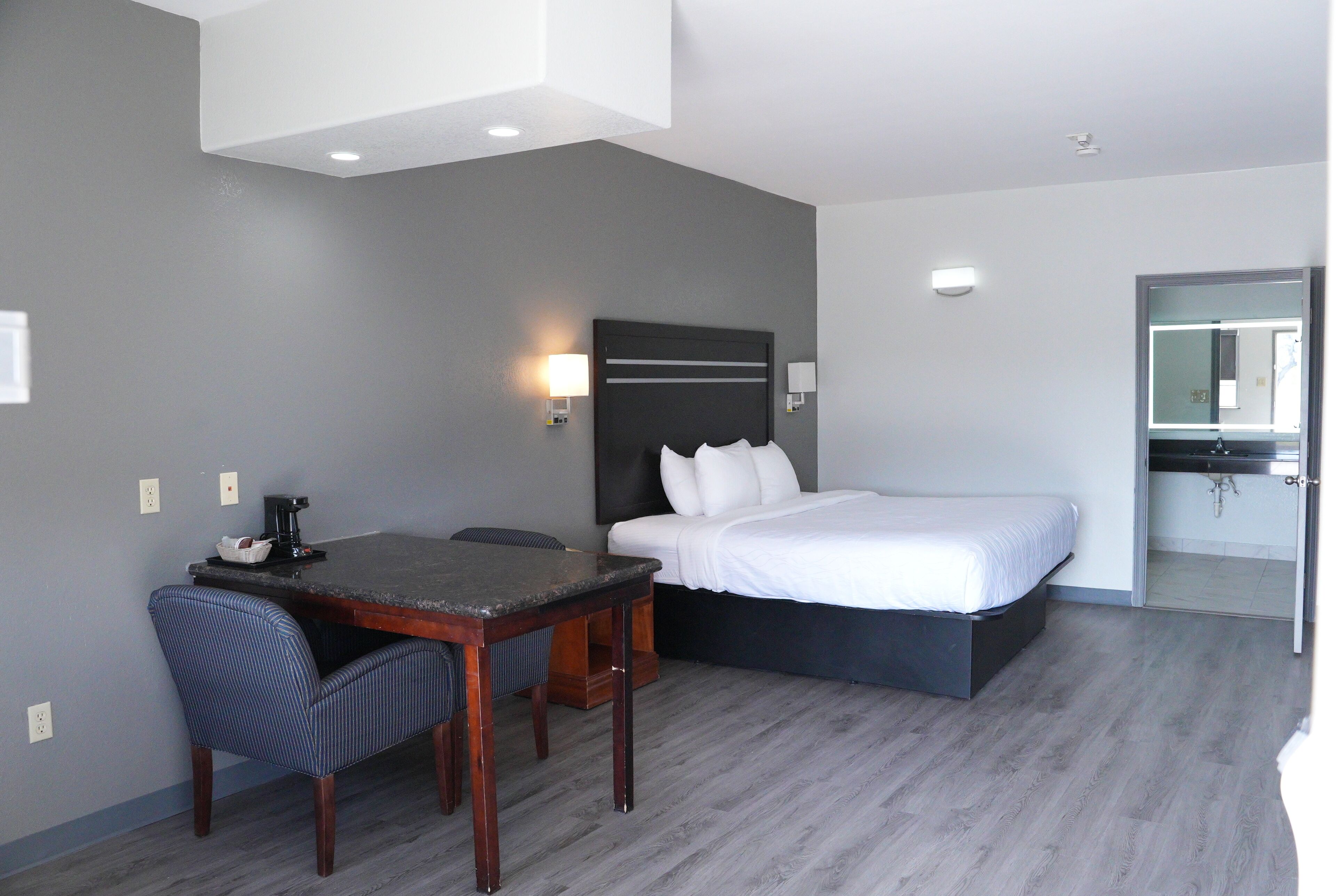 A hotel room with a bed, a desk with a chair, a coffee maker, and a wall-mounted light.