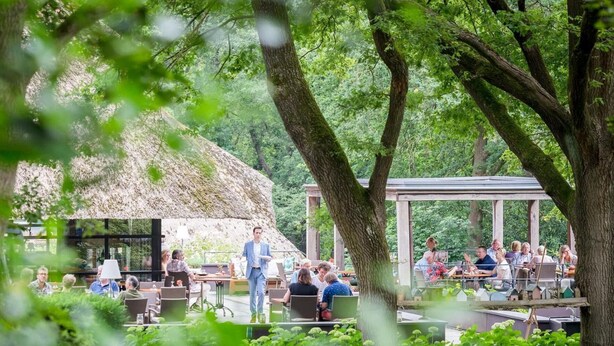 An outdoor dining area with tables and chairs, surrounded by lush greenery and trees. - Restaurant & Hotel Hoog Holten (Holten)