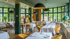 A restaurant with multiple tables and chairs, large windows, and hanging lamps. - Restaurant & Hotel Hoog Holten (Holten)