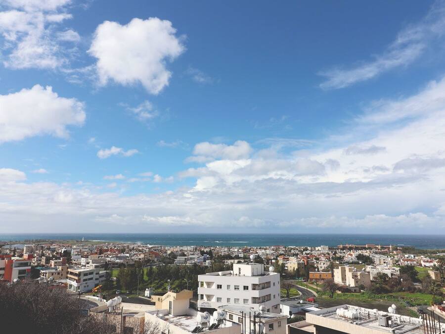 Un paysage urbain côtier, avec un mélange de bâtiments résidentiels et commerciaux, un ciel dégagé et une vue sur la mer.