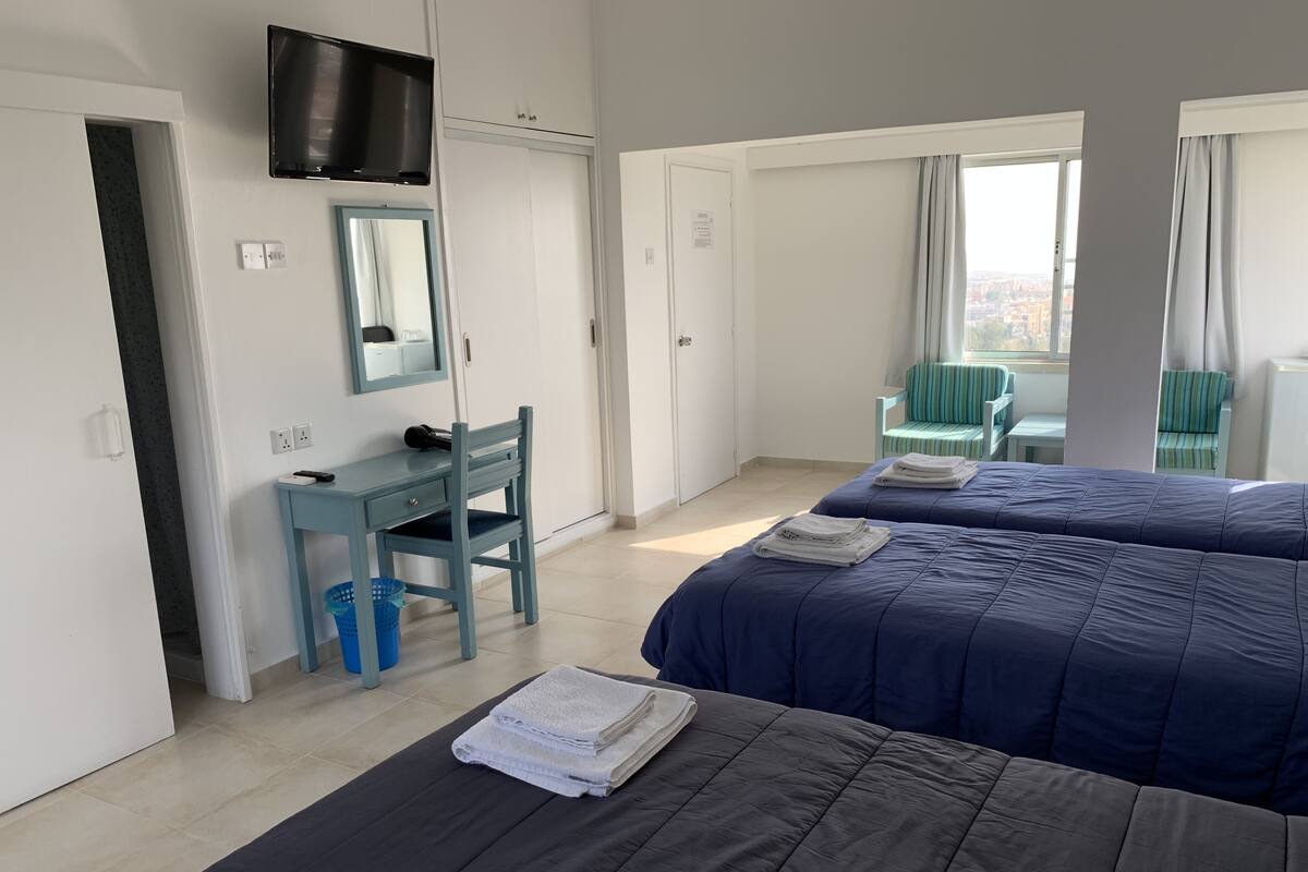 Une chambre d’hôtel avec deux lits, un bureau, une chaise, une télévision et une fenêtre donnant sur un beau paysage.