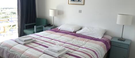 A hotel room with a bed, two bedside tables, a chair, a window with curtains, and a painting on the wall.
