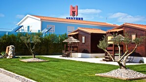 A hotel with a blue facade, a red-tiled roof, and a sign that reads 'NEPTUNO'. There are outdoor seating areas with umbrellas and a small pool. - Neptuno (Peniche)