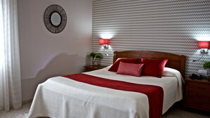 A neatly made bed with a red and white bedspread, two bedside tables with lamps, a wall-mounted mirror, and a patterned wallpaper. - Neptuno (Peniche)