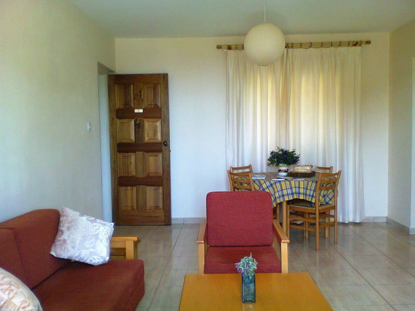 Una sala de estar con un sofá rojo, una mesa de madera y una zona de comedor con mesa y sillas.