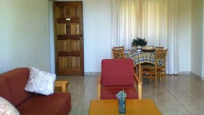 A living room with a red sofa, a wooden table, and a dining area with a table and chairs. - Aurora Apartments (Pegeia)