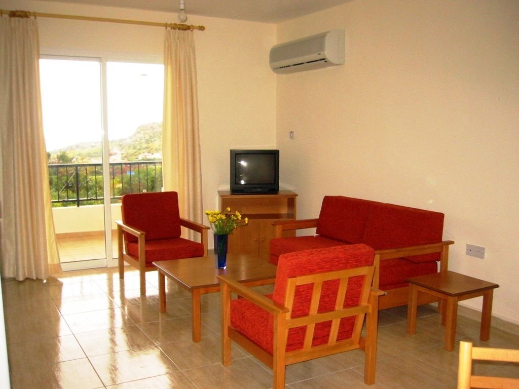 Una sala de estar con un sofá, dos sillones, una mesa de centro y un televisor sobre un mueble de madera.