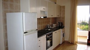 A compact kitchen with white cabinets, a refrigerator, a sink, a coffee maker, and a washing machine. - Aurora Apartments (Pegeia)