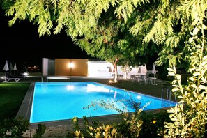 Una piscina rodeada de vegetación, con mobiliario exterior y un edificio al fondo.