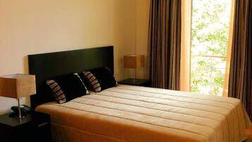 A bedroom with a bed, a nightstand, a lamp, and a window with curtains.