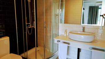 Un baño con ducha de vidrio, lavamanos blanco y retrete.