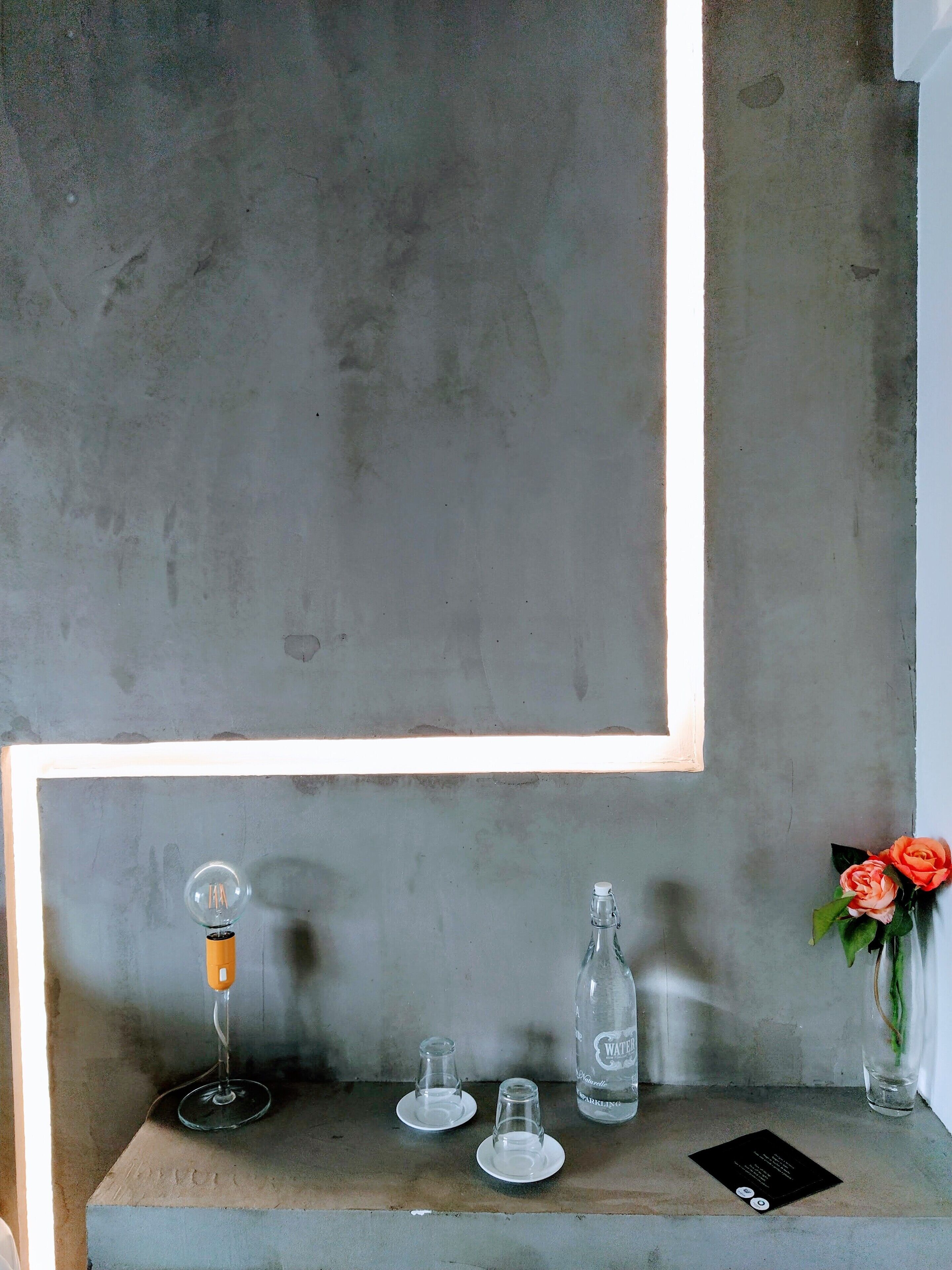 A minimalist table setup with a wine glass, two clear glasses, a bottle, and a vase with flowers.