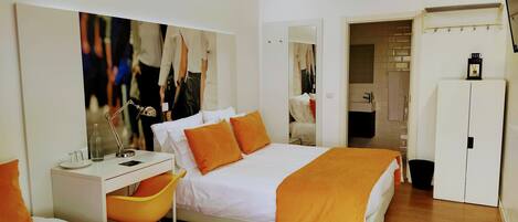 Una habitación de hotel con cama, escritorio, silla, armario y baño visible a través de una puerta abierta.