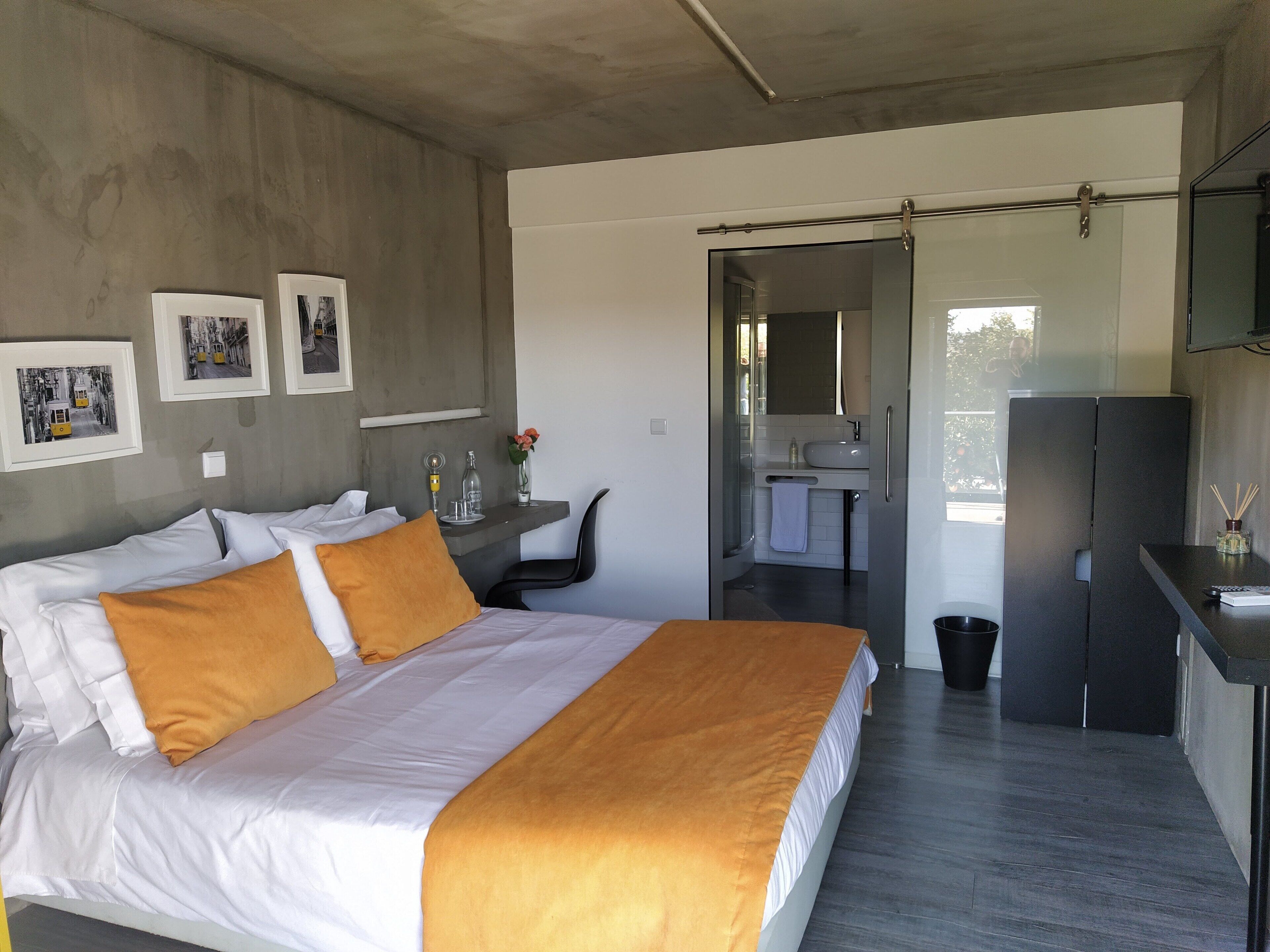 Una habitación de hotel moderna con una cama grande, un escritorio con silla, un baño y un televisor montado en la pared.
