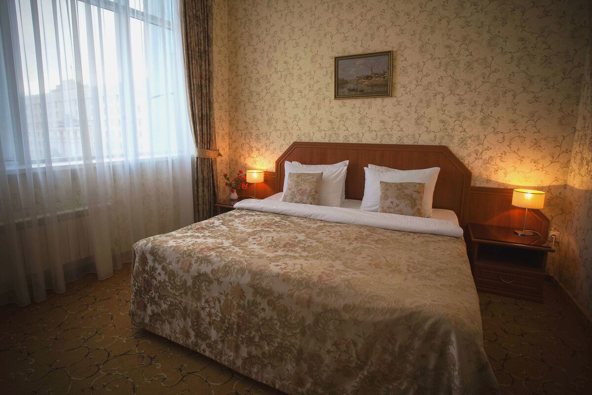Une chambre d’hôtel avec un grand lit, deux tables de chevet avec des lampes, un papier peint à motifs floraux et un tableau au mur.