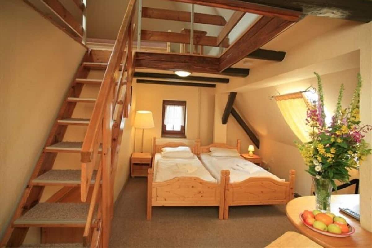 Een slaapkamer met een houten bed, een nachtkastje, een lamp, een raam, een trap en een schaal met fruit.