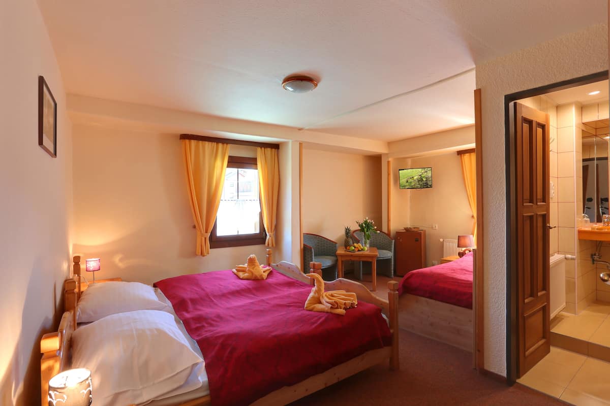 Een hotelkamer met twee bedden, een kleine tafel met een schaal fruit, een televisie en een badkamer die door een open deur zichtbaar is.