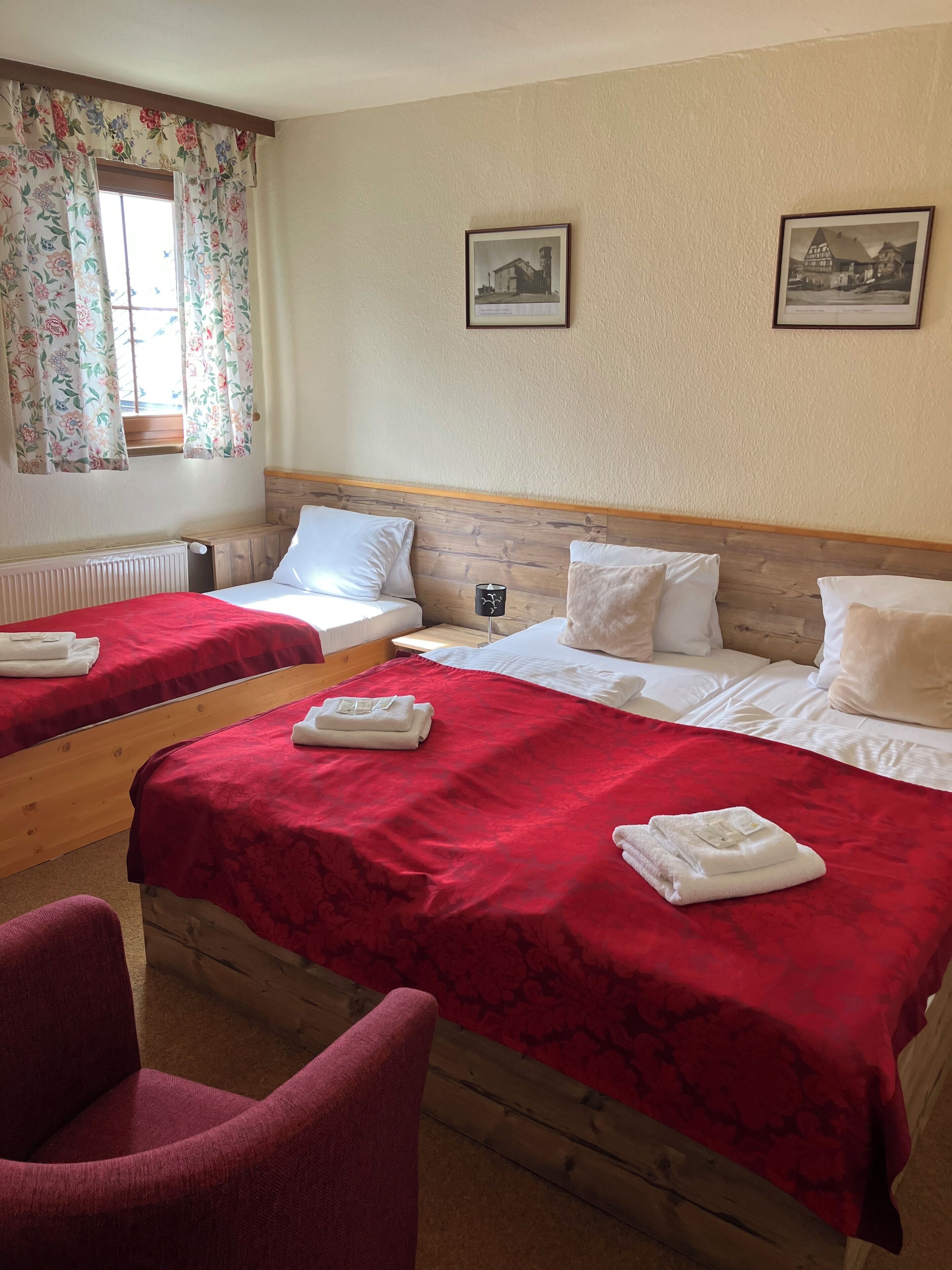Una habitació d'hotel amb dos llits, un capçal de llit de fusta, cortines florals i dos quadres penjats a la paret.