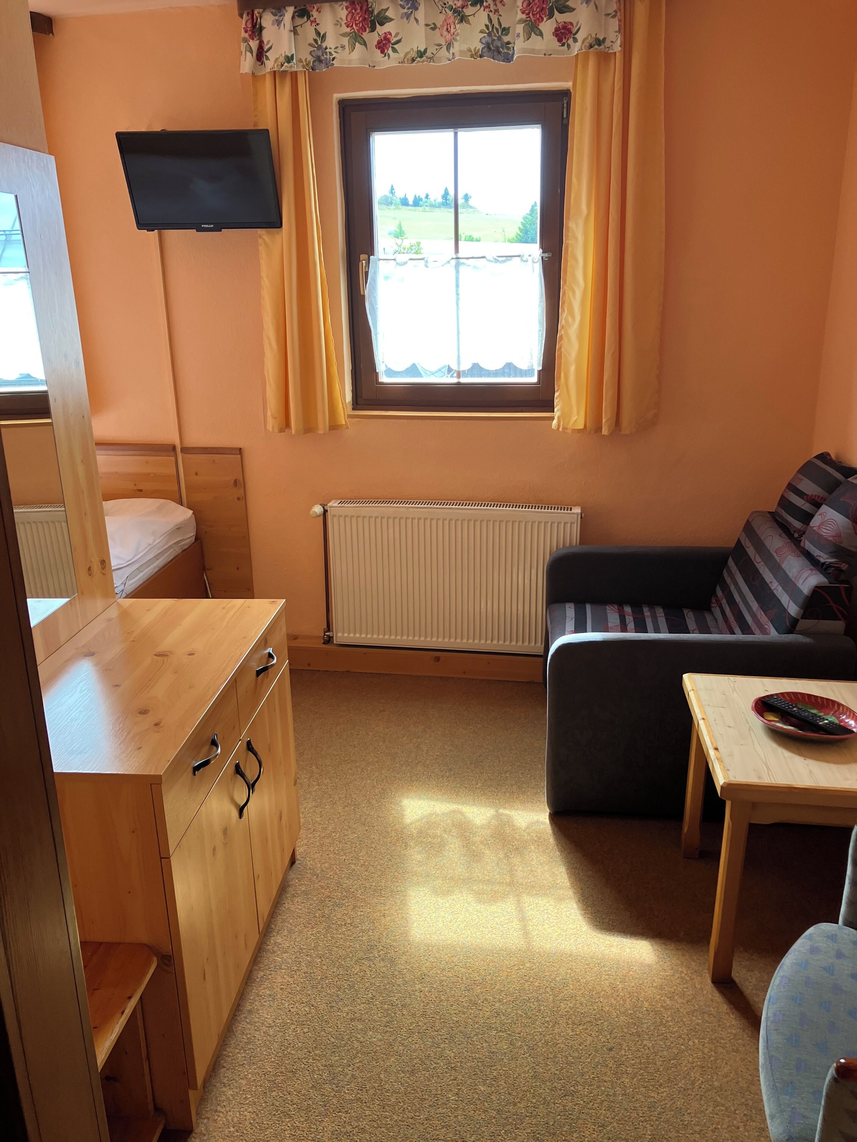 A compact room with a bed, a sofa, a small table, a TV, and a window with curtains.