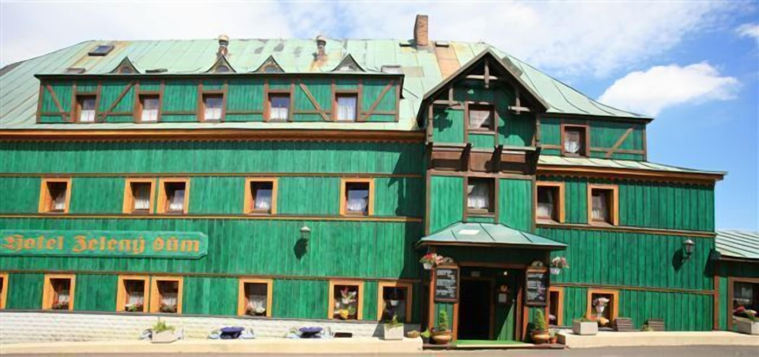 Ein großes, grünes Gebäude mit einem Schild, auf dem „Hotel Zelensky“ steht. Es hat zahlreiche Fenster und einen markanten Eingangsbereich mit einer kleinen Veranda.