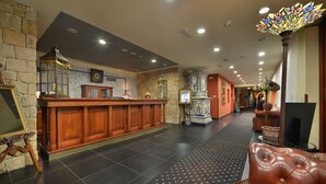 A lobby with a reception desk, a stone wall, a patterned floor, and a large decorative lamp. - Golf hotel Morris (Marianske Lazne)