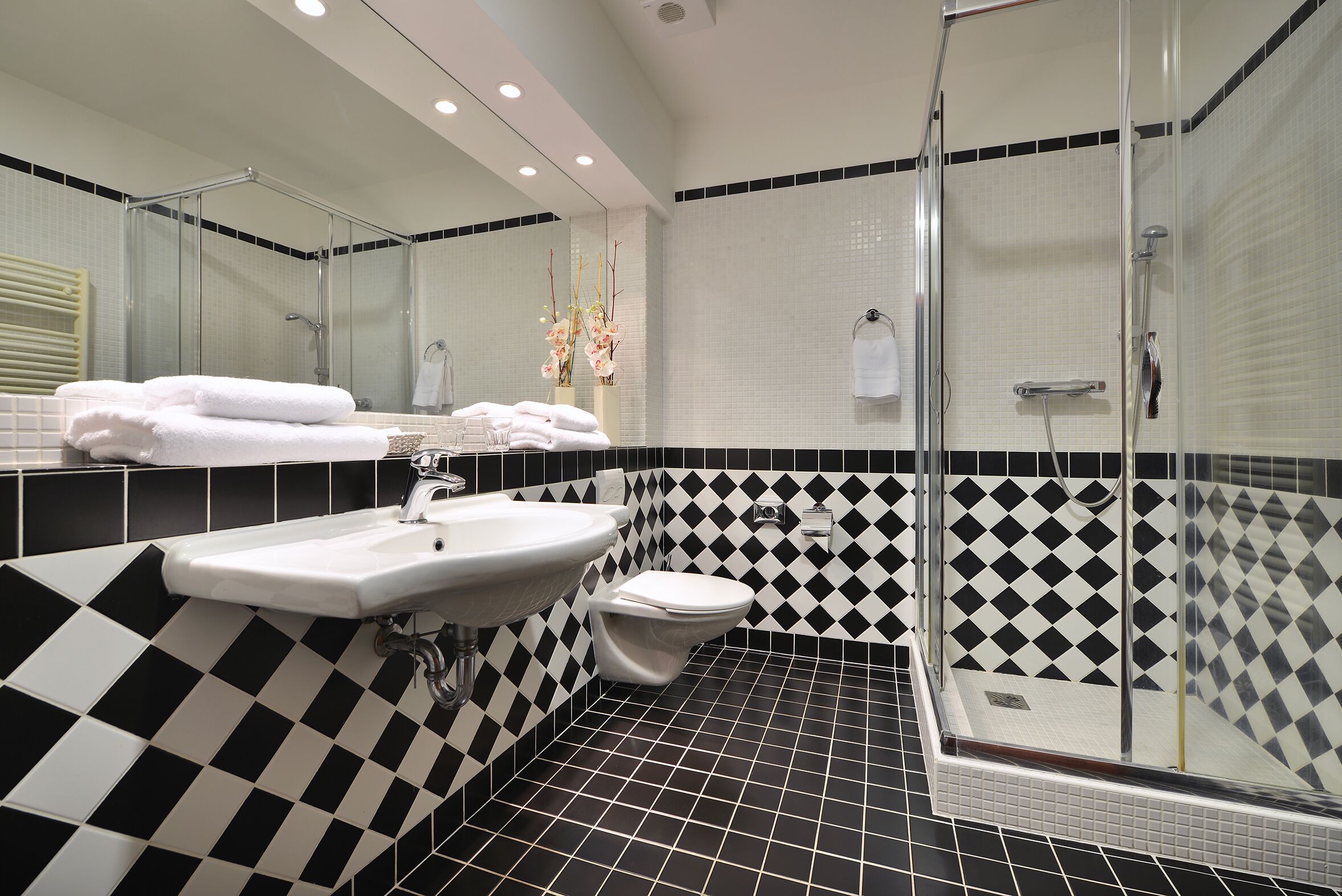 A bathroom with a black and white checkered floor, a sink, a toilet, and a glass-enclosed shower area.
