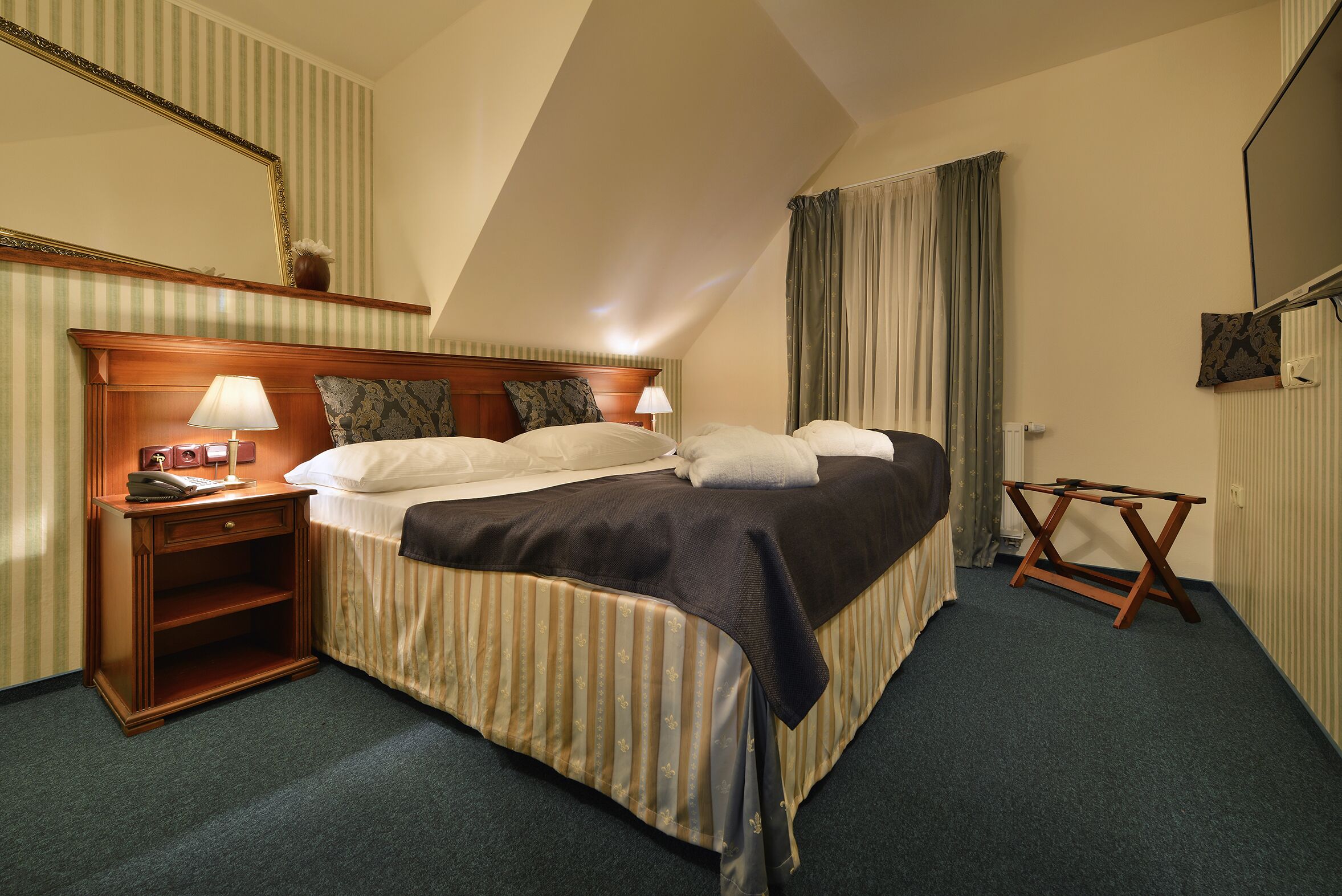 Una camera d'albergo con un letto, comodini, uno specchio e una finestra con tende.