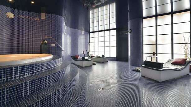 A spa area with a large bathtub, seating areas, and a view of the outdoors through large windows. - Golf hotel Morris (Marianske Lazne)