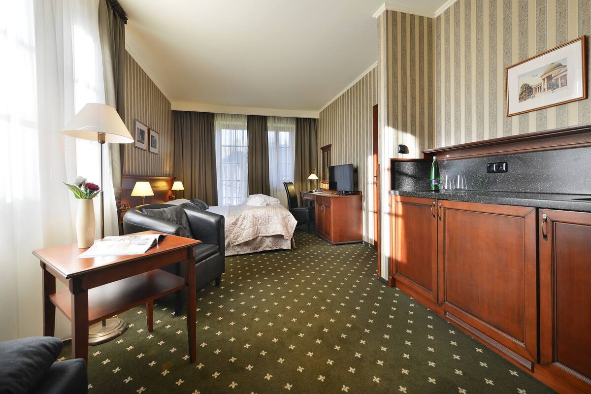A hotel room with a bed, a desk, a chair, a TV, and a minibar.