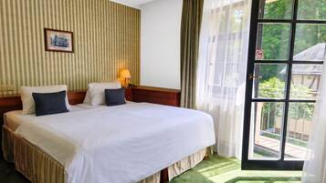A hotel room with a large bed, a bedside lamp, a framed picture on the wall, and a view of greenery through a window.