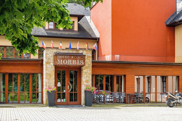 A hotel entrance with a stone facade, large windows, and outdoor seating. - Golf hotel Morris (Marianske Lazne)