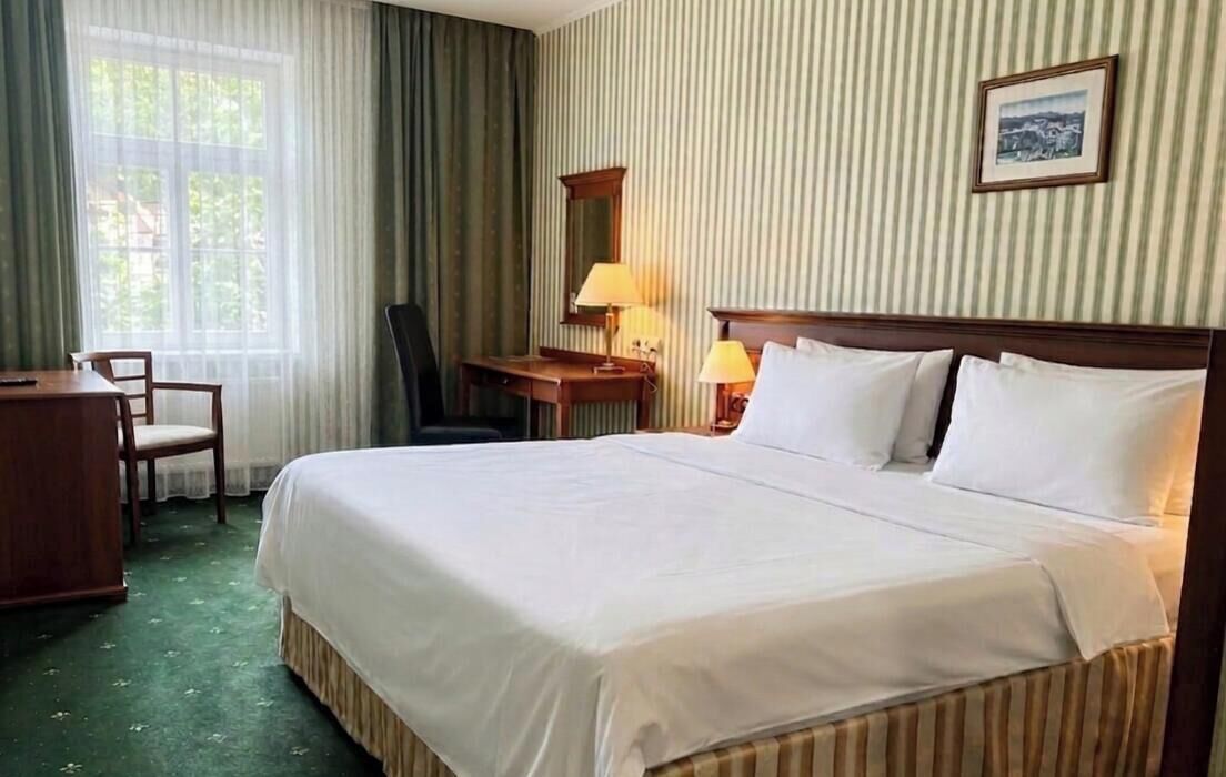 Ein Hotelzimmer mit einem großen Bett, einem Schreibtisch, einem Stuhl, einer Lampe und einem Bild an der Wand.